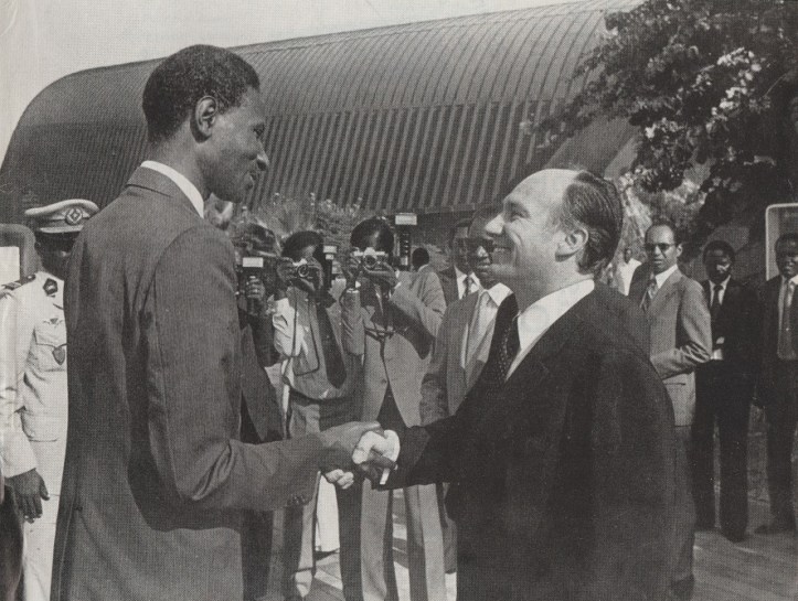 Two men shaking hands outdoors, surrounded by a crowd of photographers, possibly during a significant event.