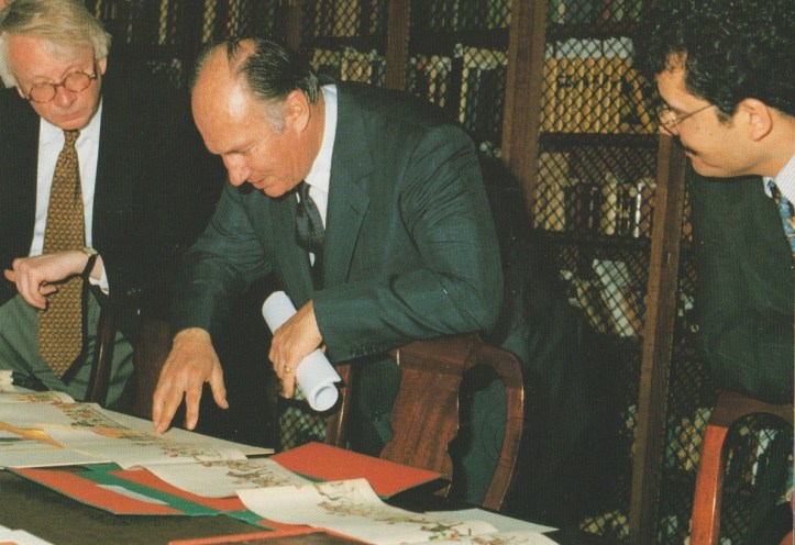 Mawlana Shah Karim, His Highness the Aga Khan IV, examines documents with two other individuals in a library setting.