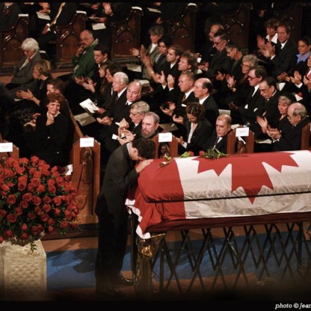 The photograph shows former Prime Minister Pierre Elliott Trudeau’s family, friends, colleagues, and official guests in attendance to observe his passing. His son, Justin, now the Prime Minister of Canada, rests his head on the casket of his father. Margaret Trudeau, in the front pew with son, Alexandre, is flanked by the beloved prime minister’s later life partner, Deborah Coyne, and their daughter, Sarah. The former prime minister’s sister, Suzette Rouleau, is on the far side of the same first row. Leonard Cohen on the right. In attendance next to Cuban President Fidel Castro are former Governor-General Romeo Leblanc, His Highness Prince Karim Aga Khan and former U.S. President Jimmy Carter. Other notables present at the ceremony not shown in this photograph include past Canadian Prime Ministers John Turner, Joseph Clark, Brian Mulroney, and Jean Chrétien. Photo: Copyright Jean-Marc Carisse.
