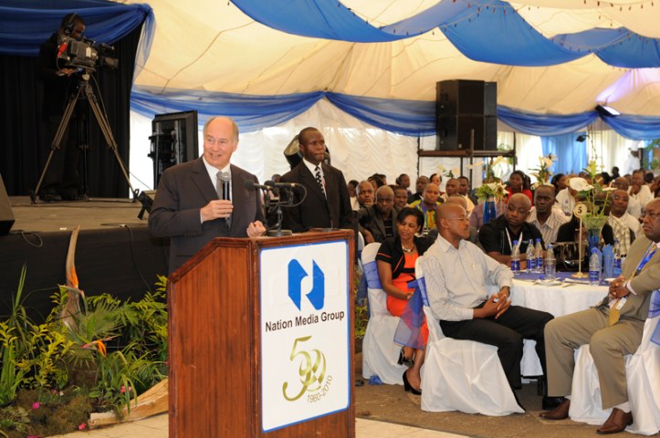 Aga Khan IV speaking at a podium during the 50th anniversary celebration of the Nation Media Group, with an audience gathered in a decorated marquee.