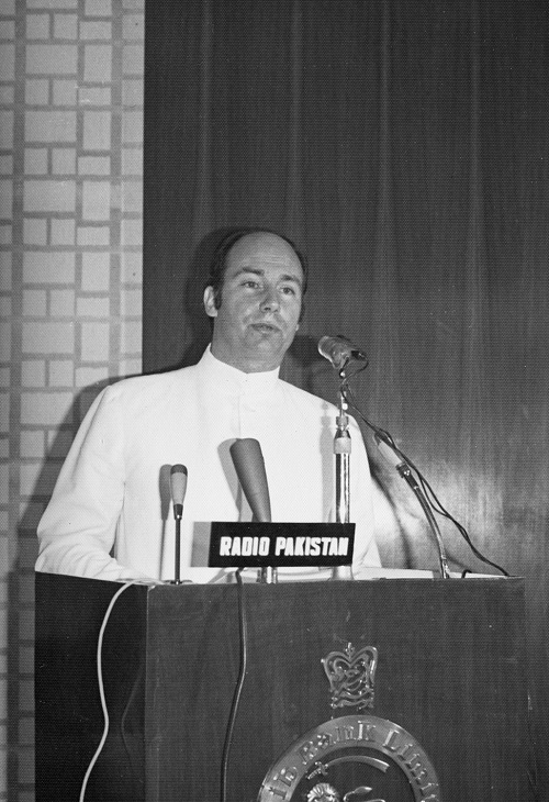 Black and white photograph of a man speaking at a podium labeled 'RADIO PAKISTAN', dressed in a formal white outfit.