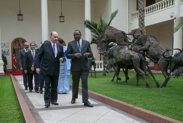 Mawlana Shah Karim, His Highness Aga Khan IV, walking alongside Kenyan President Uhuru Kenyatta in a garden area, with sculptures of animals in the background.