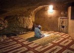 A person sitting on a prayer mat inside a cave, with a soft light illuminating the space.