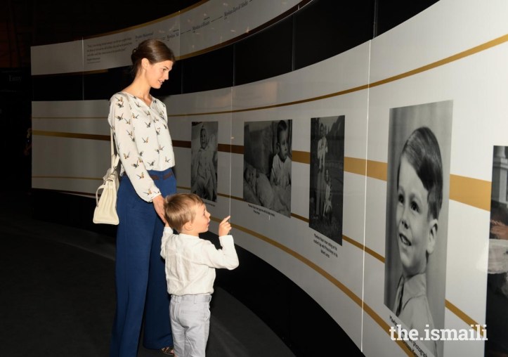 A woman and a young boy looking at historical photographs displayed on a wall at an exhibition.