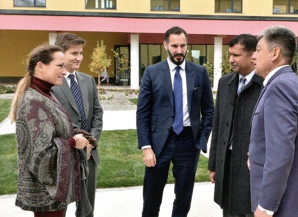 A group of five individuals in formal attire engaging in conversation outdoors, with a modern building in the background.