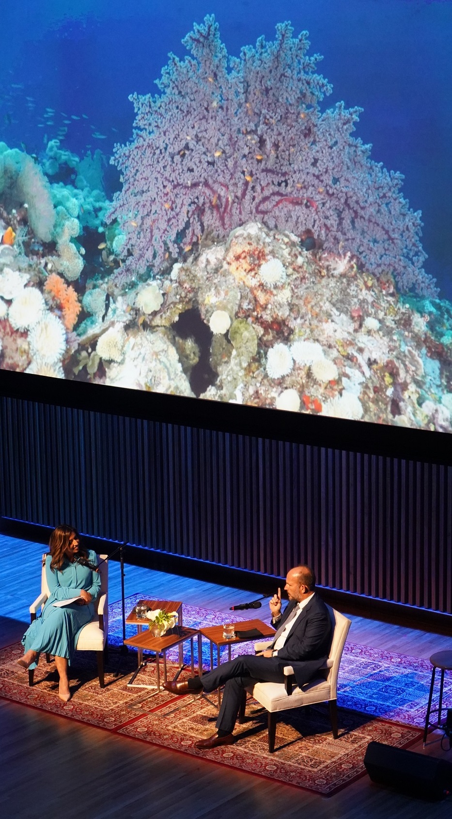 A photograph of a coral reef taken by Prince Hussain Aga Khan during one of his dives into the ocean is projected on the screen as Farah Nasser engages the Prince in a conversation during his presentation of The Living Sea - Fragile Beauty at the Aga Khan Museum; May 24, 2023. Photograph