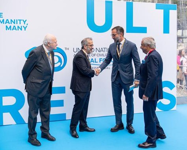 Four men in formal attire engaged in a handshake and conversation at a United Nations event, standing in front of a blue-themed backdrop with the words 'ULT' and 'RES'.