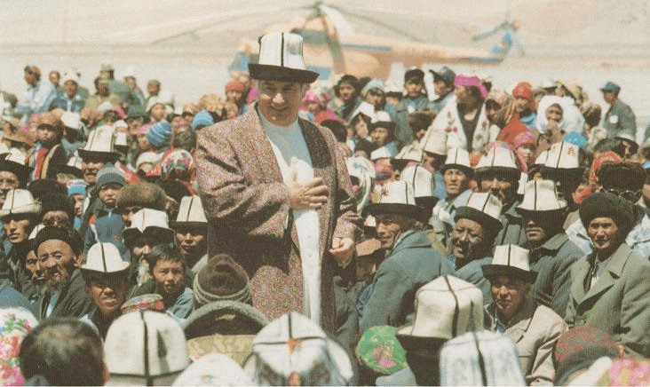 Mawlana Shah Karim, His Highness the Aga Khan IV, speaking to a large gathering of Ismaili followers wearing traditional hats in a mountainous region.