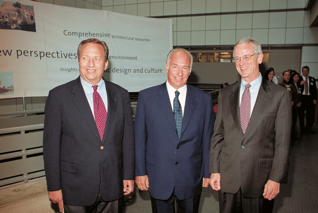 Three men posing for a photo at an event, with a banner in the background promoting architectural resources and cultural insights.