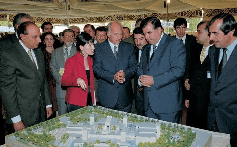 Group of people discussing a architectural model during an event, with notable figures present in the scene.