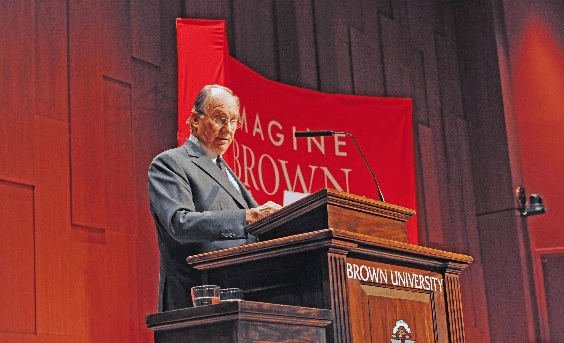 His Highness the Aga Khan delivering a speech at Brown University, with a red 'Imagine' banner in the background.