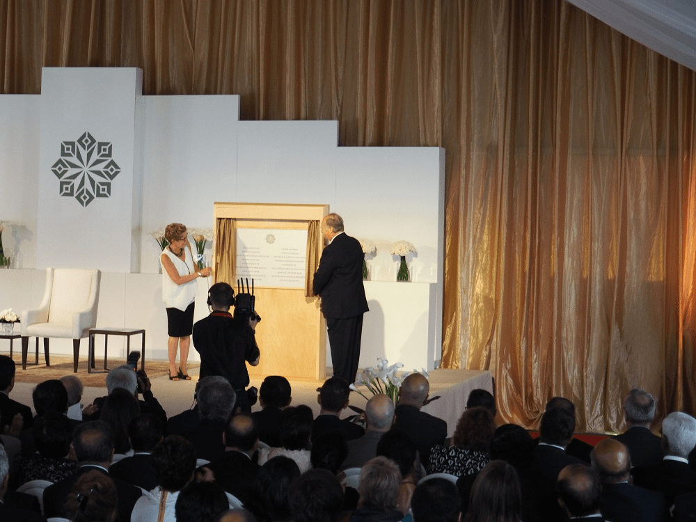 Aga Khan IV unveils a plaque during a ceremony at an elegant venue, with an audience seated in front, highlighting the event's significance.