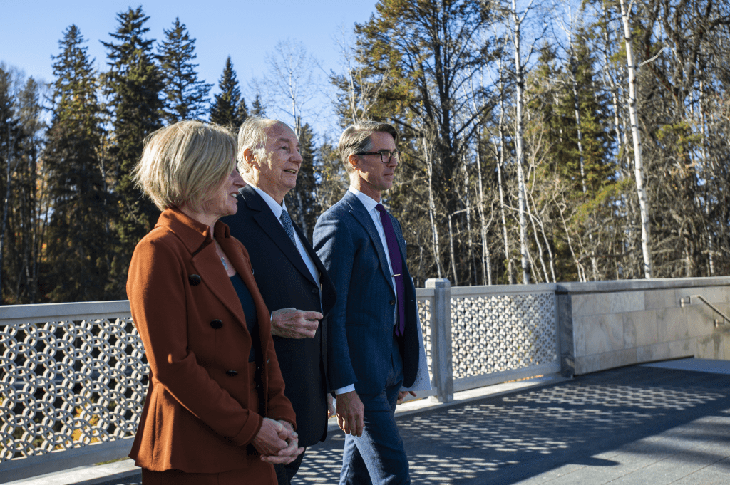 Three individuals walking together on a bridge surrounded by trees in a forested area.
