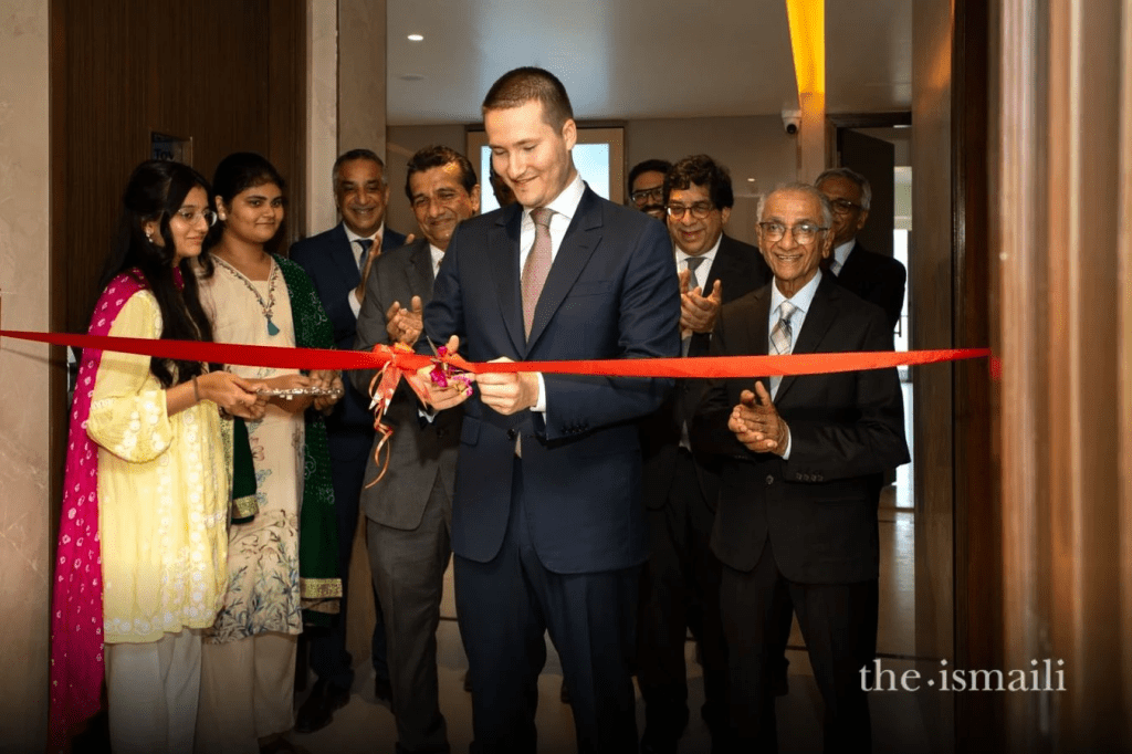 A group of people gathered for a ribbon-cutting ceremony, with a man in a suit cutting the red ribbon while others applaud and celebrate.